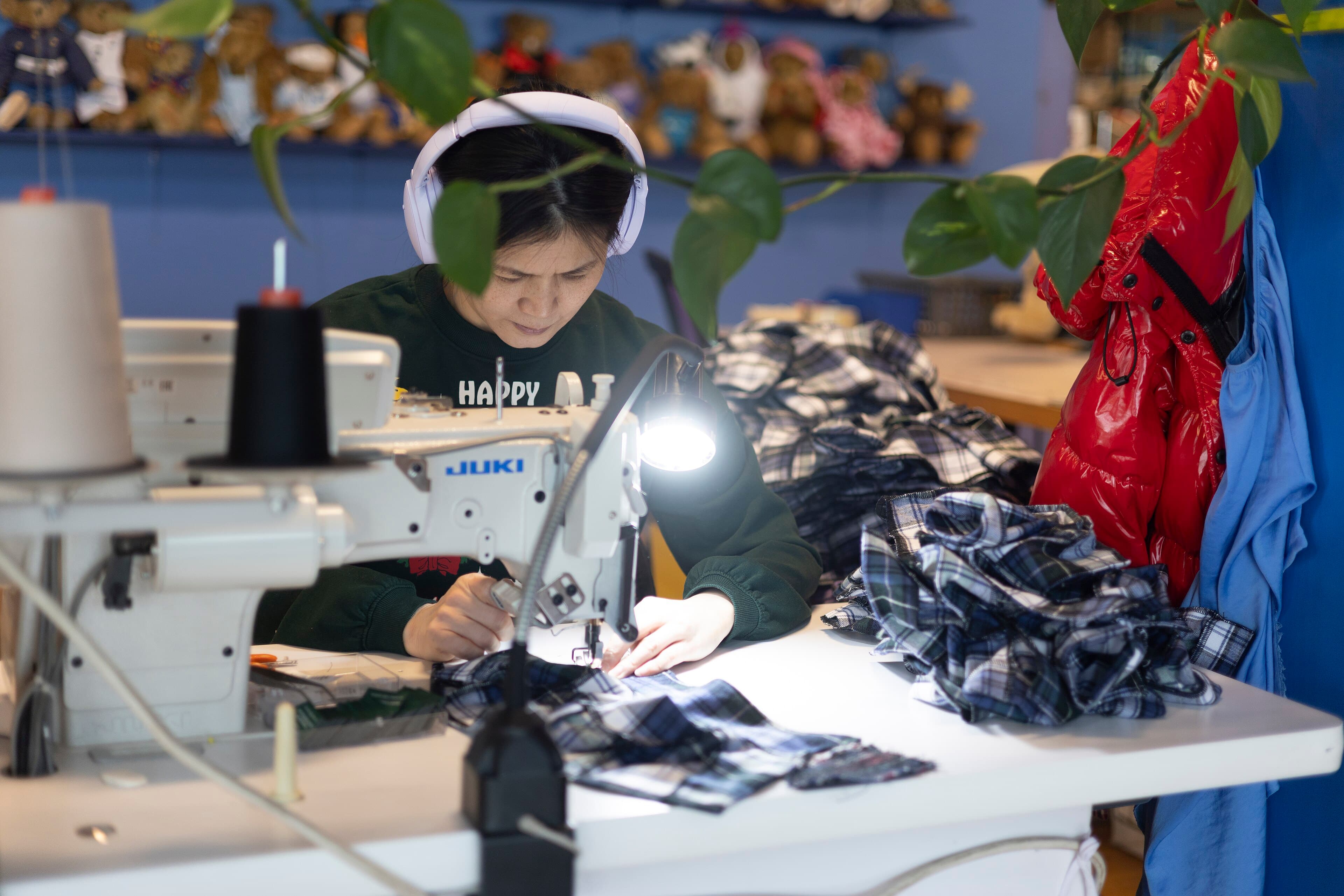 A worker sewing fabric components on an industrial sewing machine in a factory